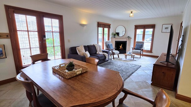 A spacious living room with a fireplace, a dining area with a wooden table, and a television. - Sandstone Suites (Port Fairy)
