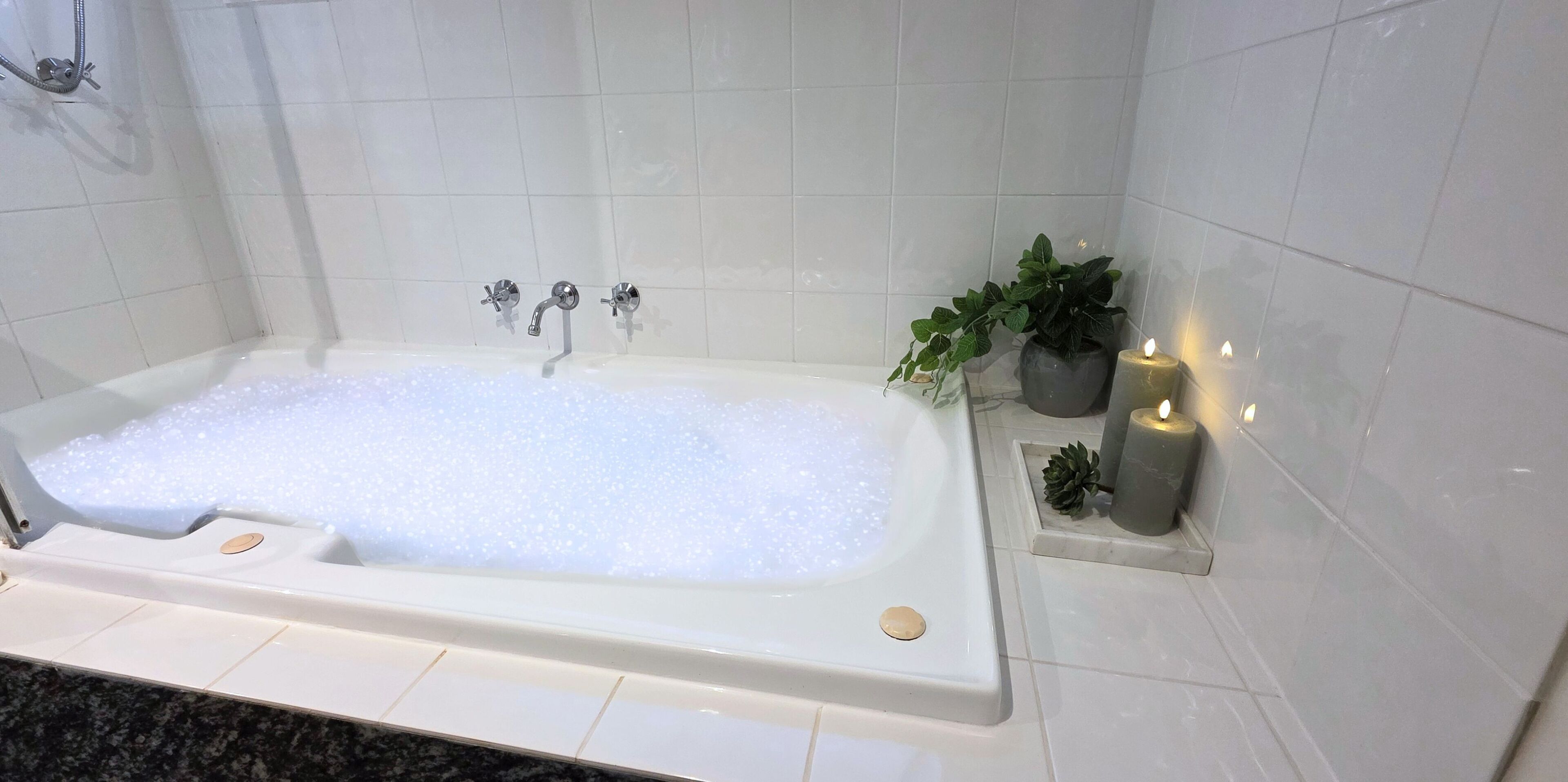 A modern bathroom with a large bathtub filled with bubbles, a showerhead, and a potted plant.