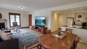 A living room with a fireplace, sofa, TV, and a dining area with a table and chairs. - Sandstone Suites (Port Fairy)