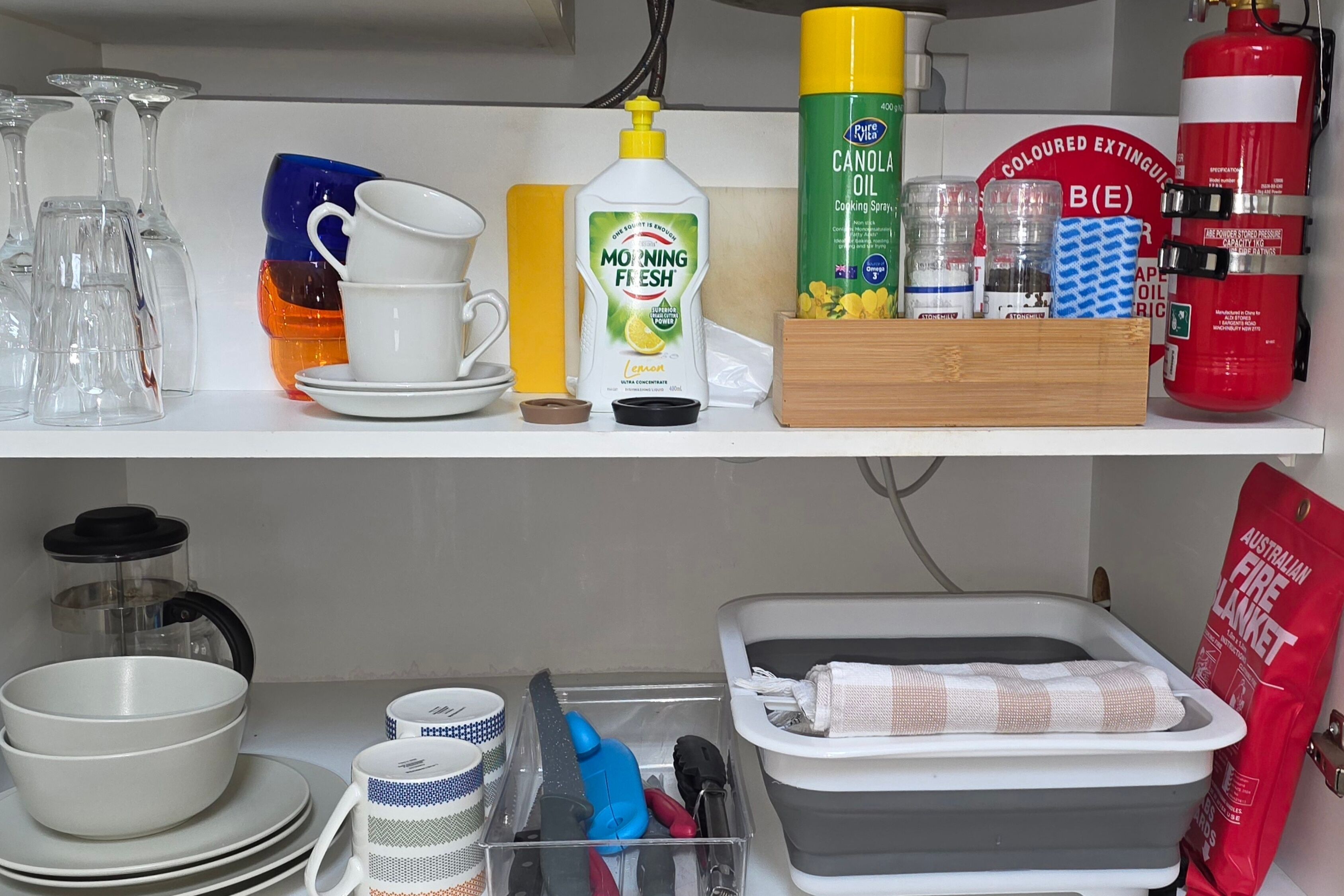 Une étagère de cuisine contenant divers objets, notamment une bouteille d’huile de colza, un extincteur et une machine à café.