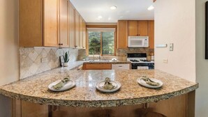 A kitchen with granite countertops, wooden cabinets, a microwave, stove, and a window providing a view of greenery. - Northstar-1.0m walk or free shuttle to the Village. Pets ok for 30+day rentals.  (Truckee)
