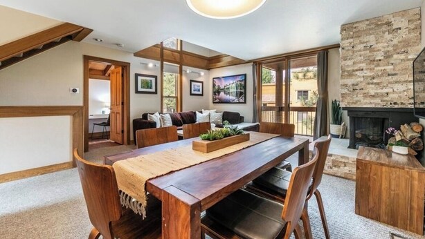 A dining area with a wooden table, chairs, and a fireplace. There is a sofa and a window with a view of the outdoors. - Northstar-1.0m walk or free shuttle to the Village. Pets ok for 30+day rentals.  (Truckee)