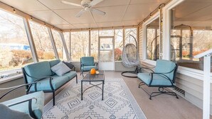 Un patio couvert avec des sièges, un ventilateur de plafond et de grandes fenêtres.