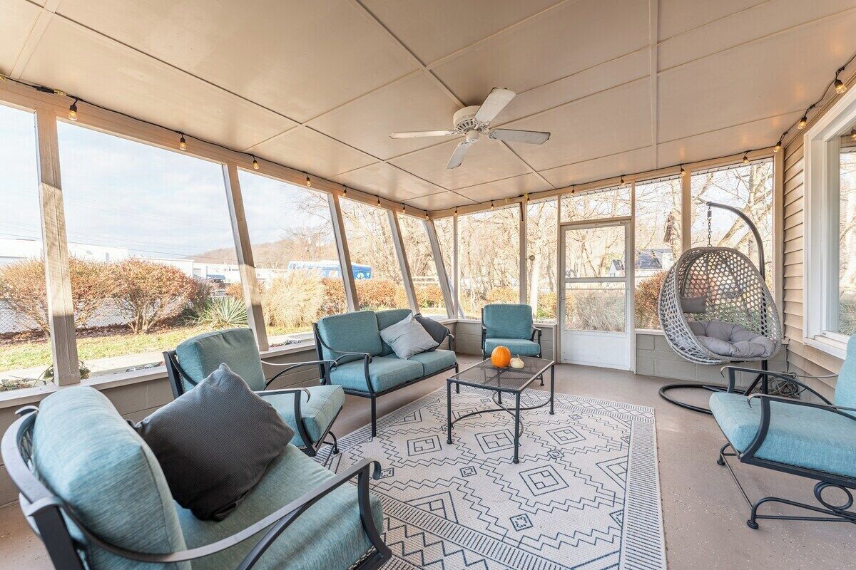 Un patio cubierto con ventilador de techo, ventanas amplias y mobiliario exterior, incluyendo una silla y un sofá.