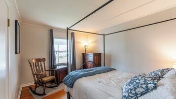 A bedroom with a four-poster bed, a rocking chair, a dresser, and a window with curtains.