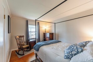 A bedroom with a four-poster bed, a rocking chair, a dresser, and a window with curtains.
