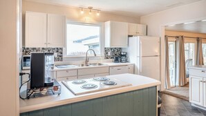 Une cuisine moderne avec des armoires blanches, une cuisinière encastrée, une machine à café et une fenêtre qui laisse entrer la lumière naturelle.