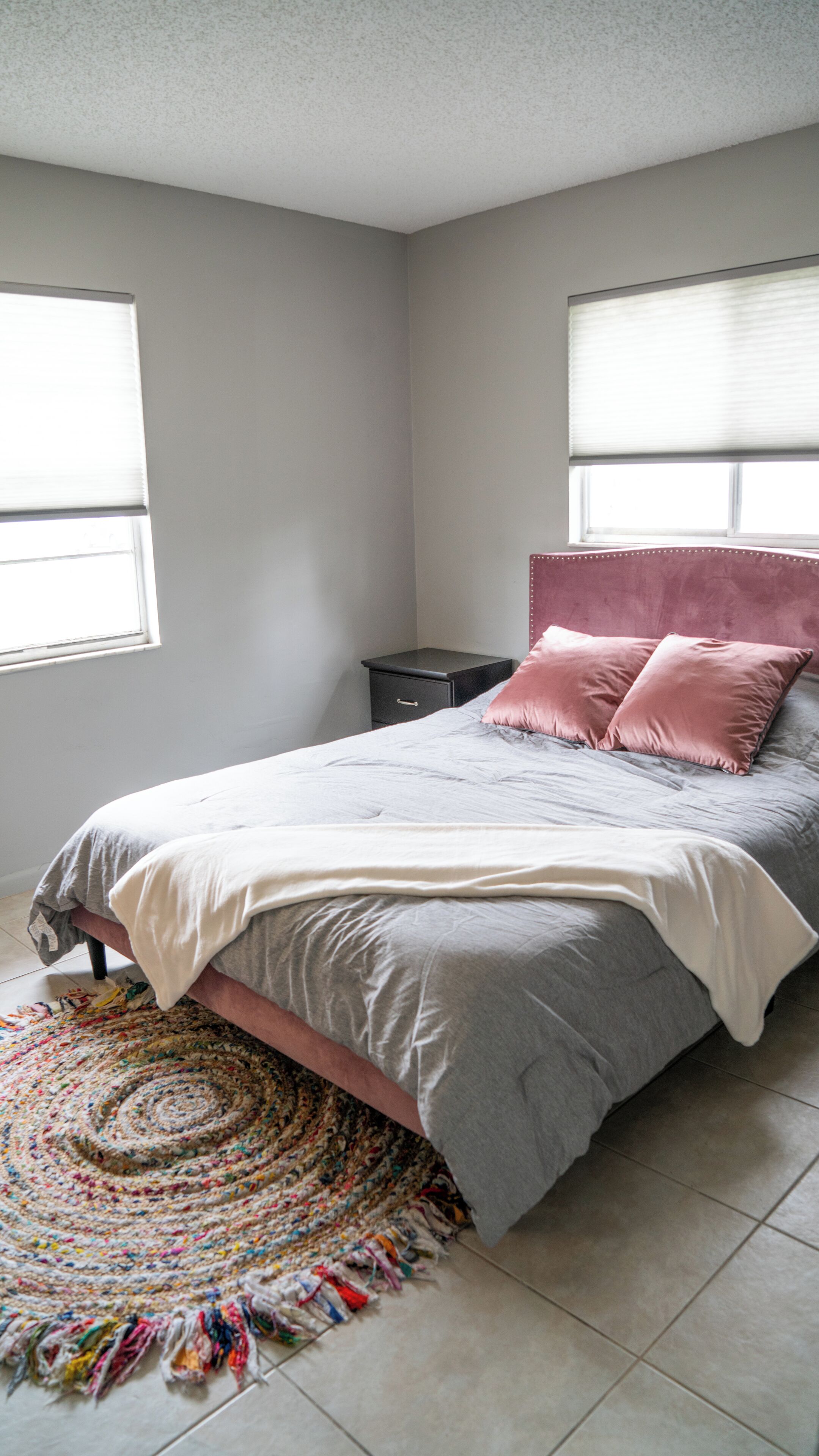 A bedroom with a bed, a nightstand, a window, and a colorful rug.