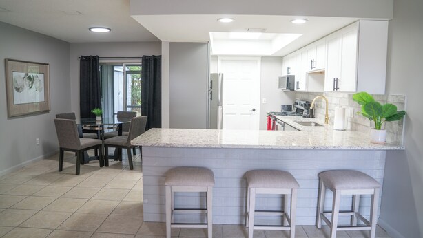 A modern kitchen with a large island, bar stools, and a dining area with chairs and a table. - Cozy 2-bedroom hideaway with WiFi, AC the heart of Fort Myers (Fort Myers)