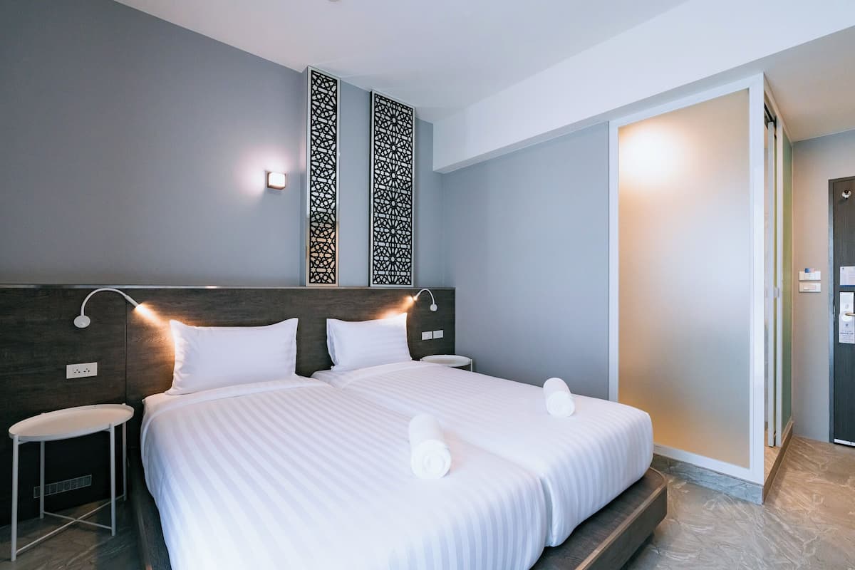 Une chambre d’hôtel moderne avec un grand lit, deux tables de chevet, un luminaire fixé au mur et un panneau décoratif.