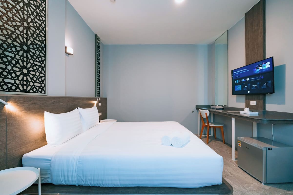 Une chambre d’hôtel moderne, dotée d’un grand lit, d’un bureau avec un ordinateur, d’un petit réfrigérateur et d’un téléviseur fixé au mur.