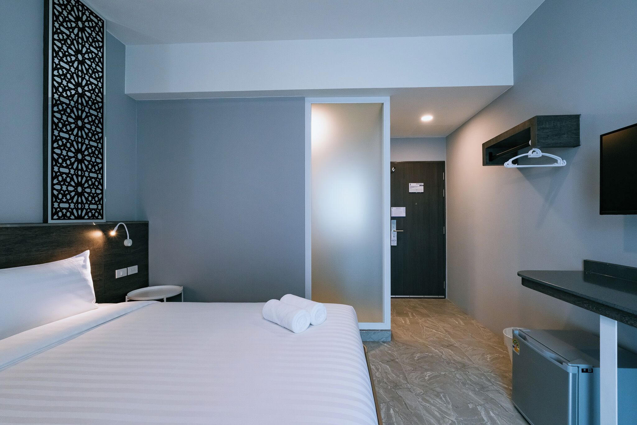 A modern hotel room with a neatly made bed, a small seating area, a walk-in closet, and a television mounted on the wall.