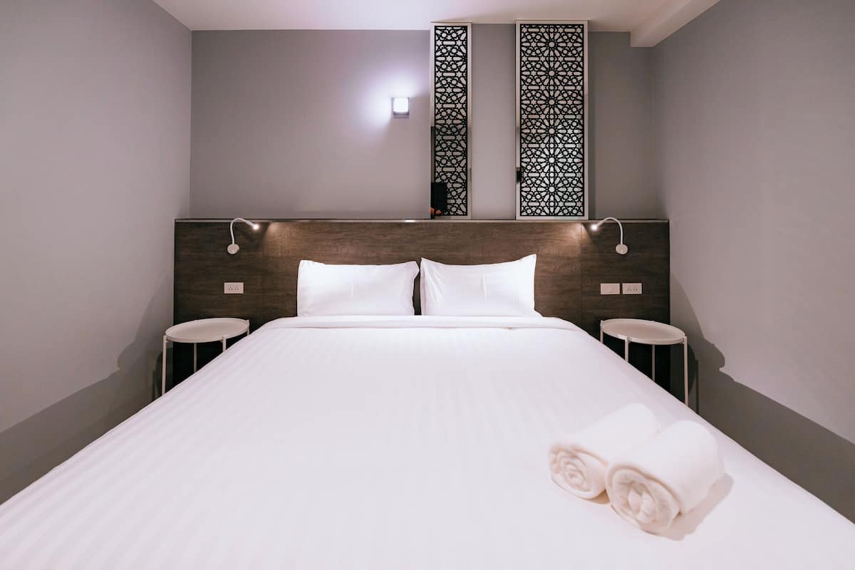 Une chambre d’hôtel avec un grand lit, deux tables de chevet, une tête de lit décorative et un luminaire fixé au mur.