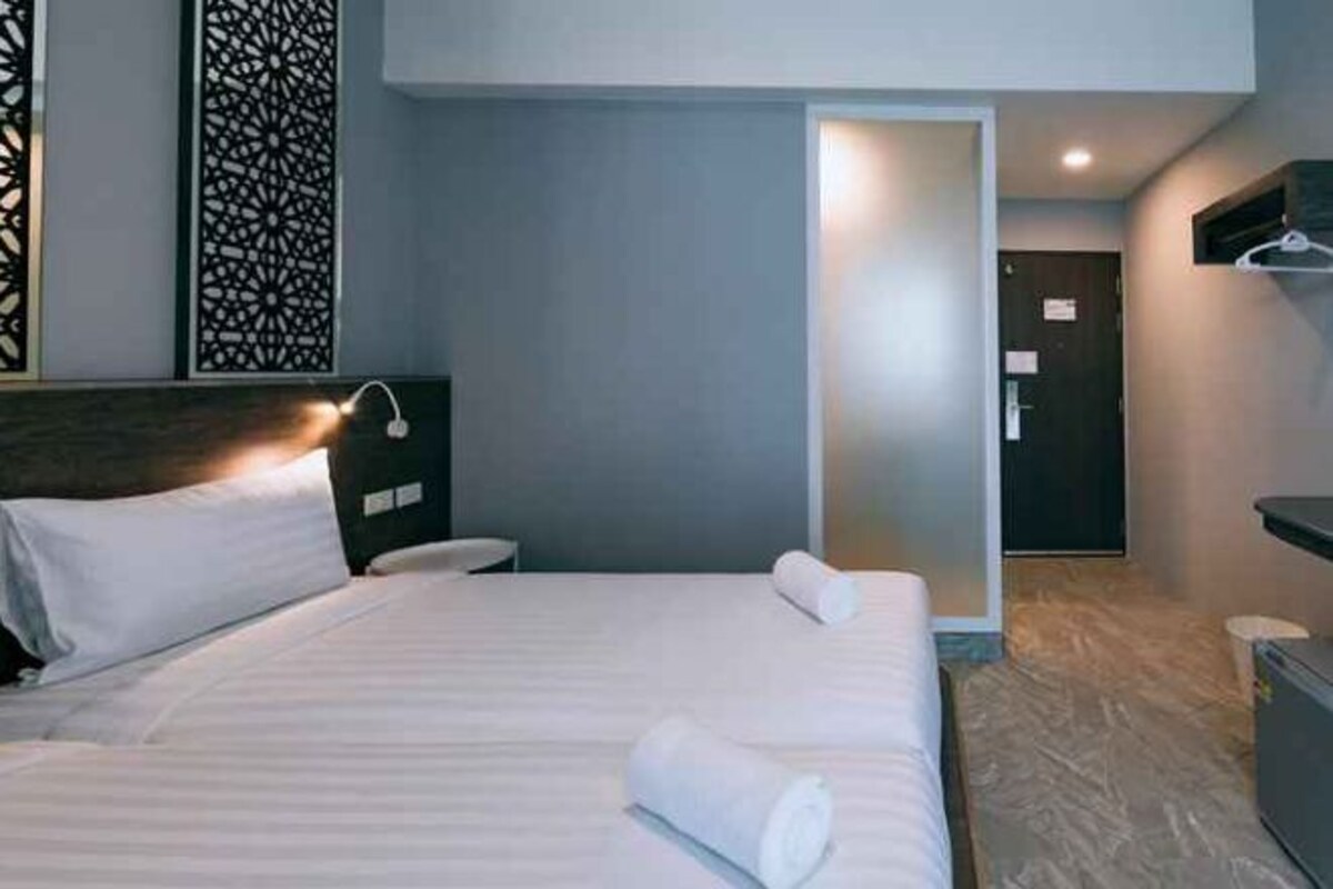 A hotel room with a bed, bedside table, and a door leading to another room.