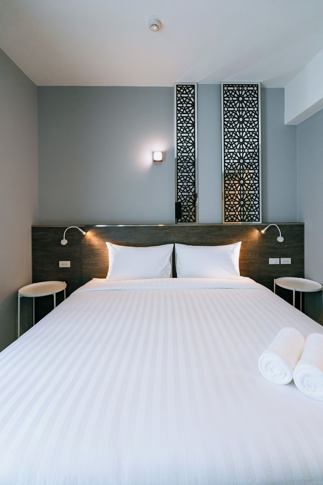 A hotel room with a large bed, two nightstands, a wall-mounted light, and decorative panels.