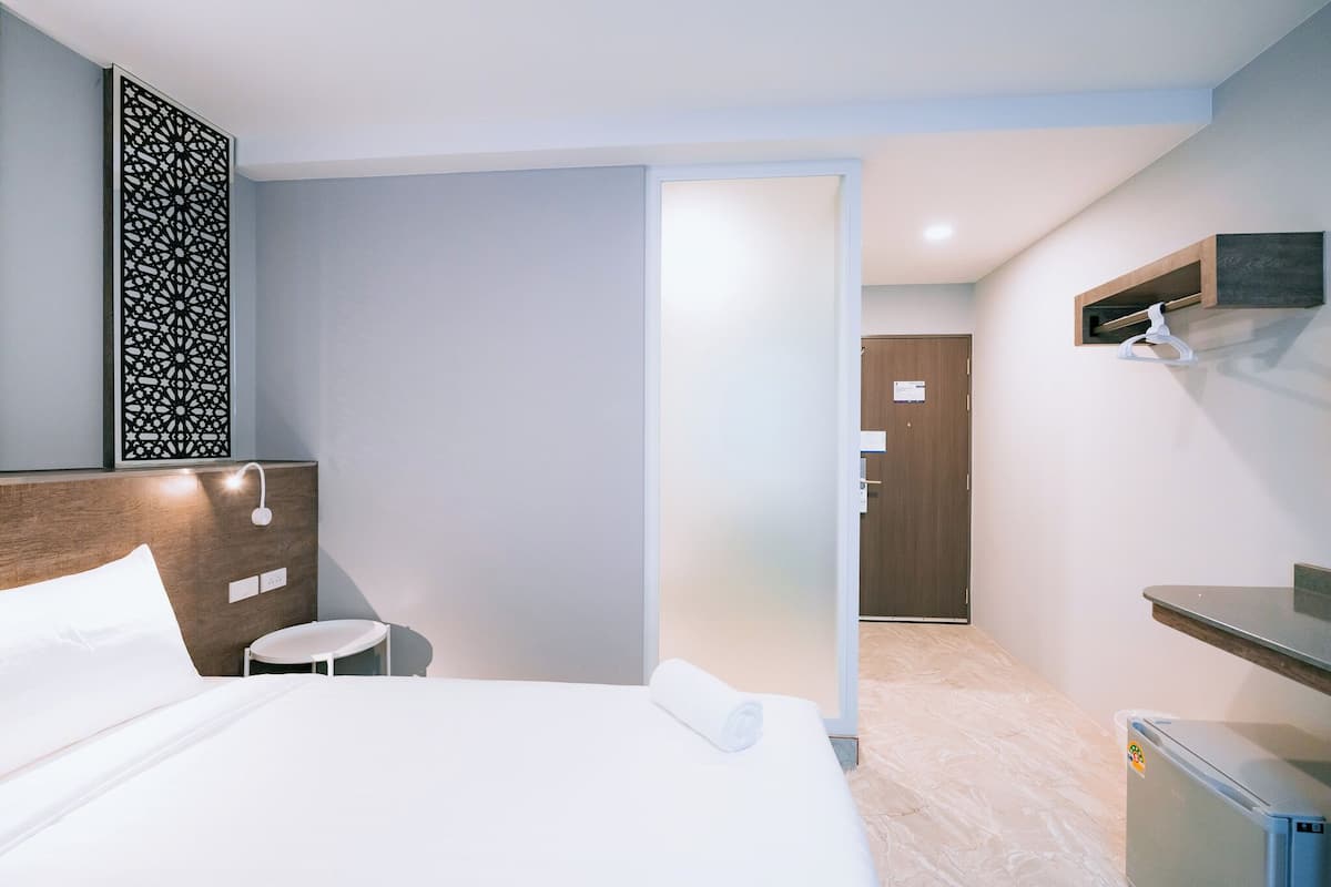 Une chambre d’hôtel comprenant un lit, une petite table, un téléviseur fixé au mur, une porte et un mini-réfrigérateur.