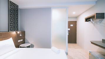 A hotel room with a bed, a small table, a wall-mounted TV, a door, and a mini-fridge.