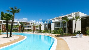 A swimming pool with lounge chairs, palm trees, and a modern building with balconies.