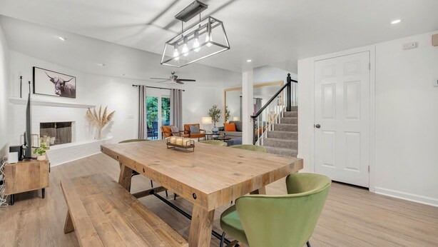 Amplia sala de estar con mesa de comedor de madera, sillas verdes, chimenea y escalera que lleva a otro nivel.