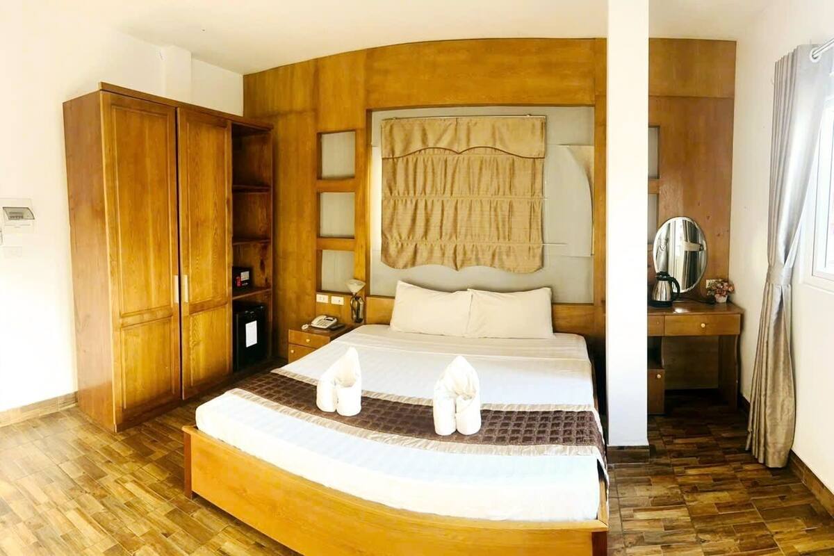A hotel room with a wooden bed, a wardrobe, a desk, and a mirror.