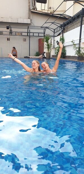 Une piscine avec deux personnes dans l’eau, dont l’une lève un bras.