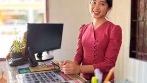 Una persona de pie detrás de un mostrador con un monitor de computadora, varios documentos y material de oficina.