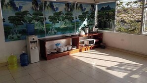 Una habitación con un ventanal grande, piso de baldosas, estante de madera con utensilios de cocina y dispensador de agua.