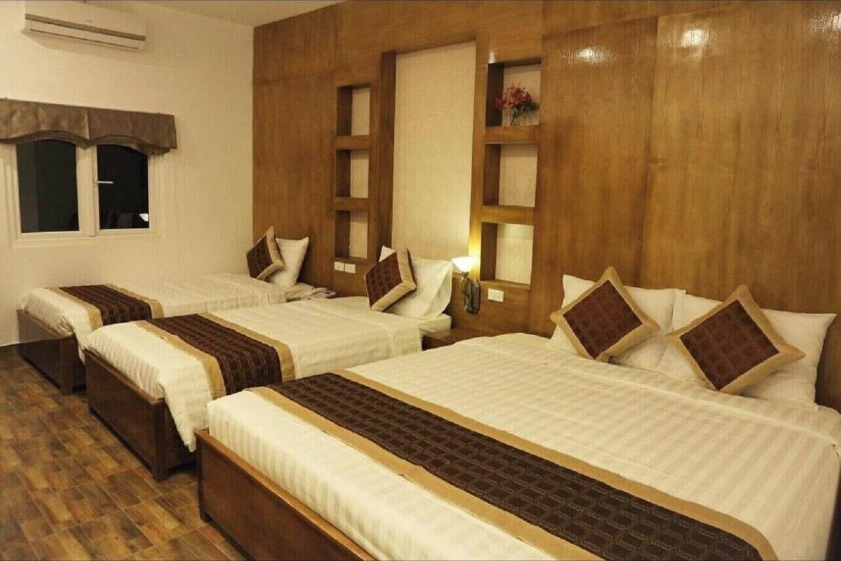A hotel room with four beds arranged in a row, each with a wooden headboard and white bedding.