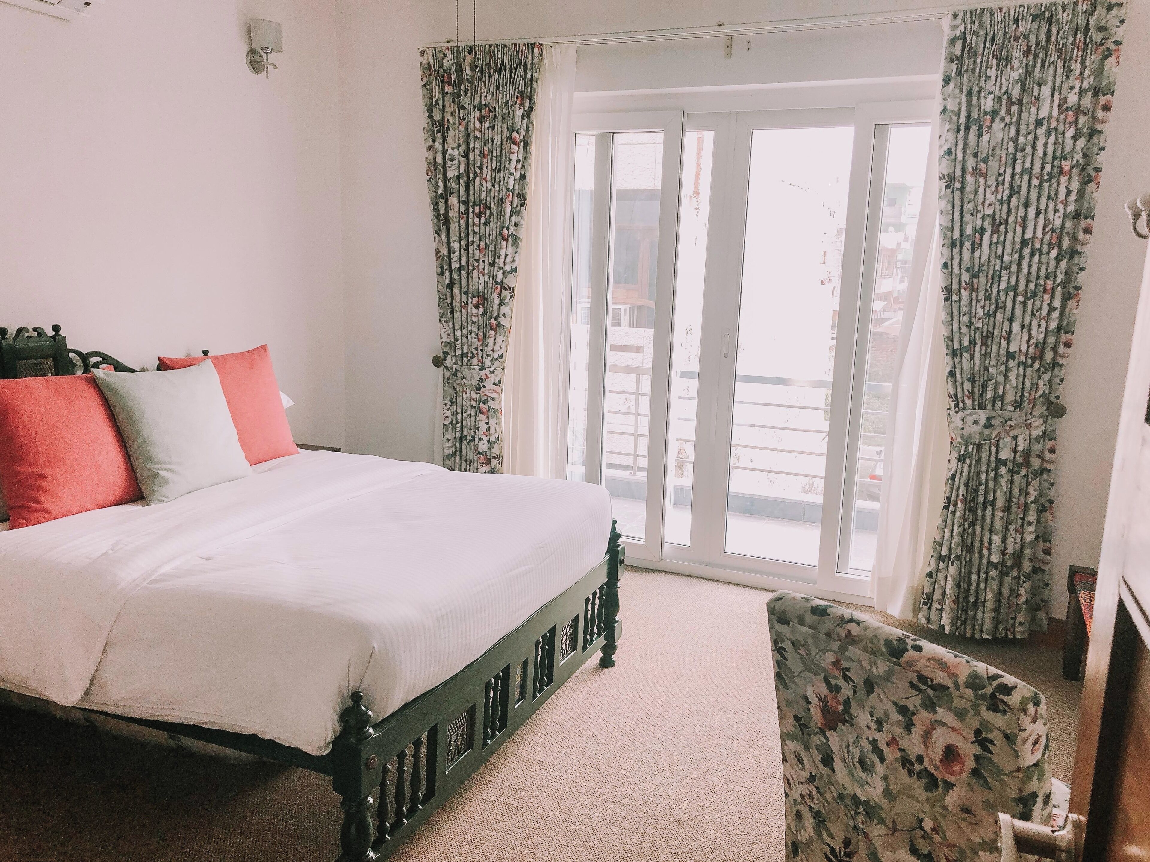 A bedroom with a bed, floral curtains, and a view of the outside.