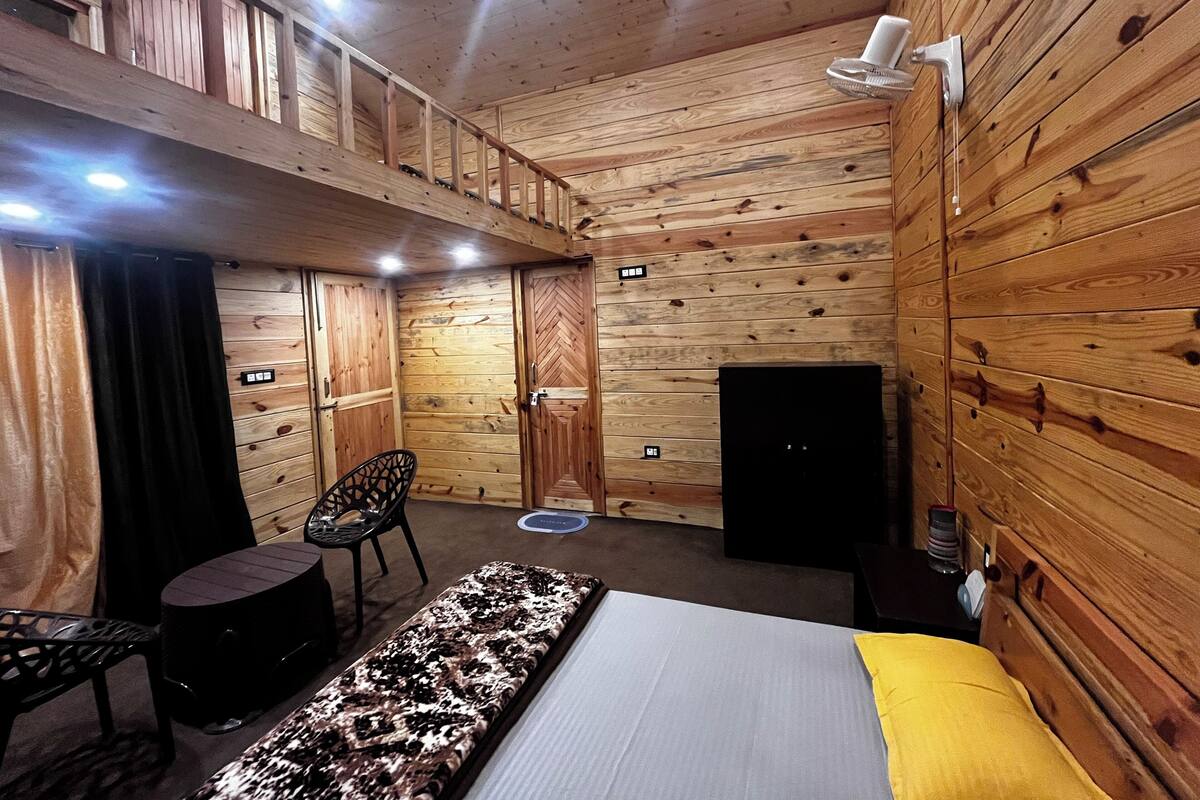 Une pièce de cabane en bois comprenant un lit, une petite table, une chaise, une cheminée et un luminaire au plafond.