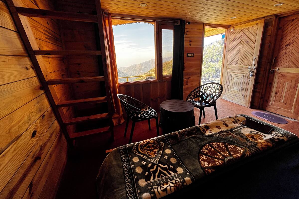 Une pièce de cabane en bois comprenant un lit, deux chaises, une petite table et une échelle.