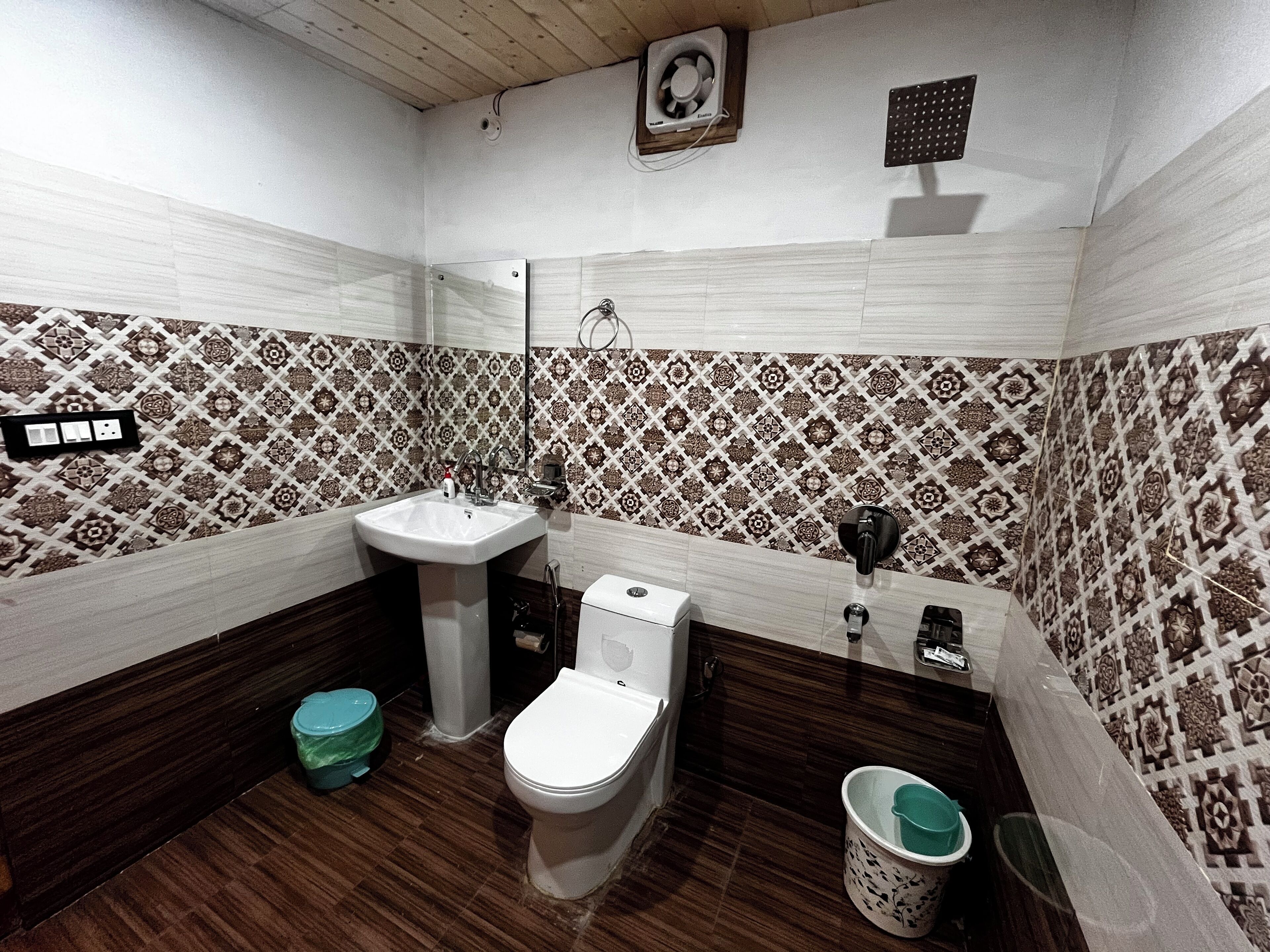A bathroom with a sink, toilet, and a mirror. There is a patterned tile backsplash, a wooden floor, and a small trash bin.
