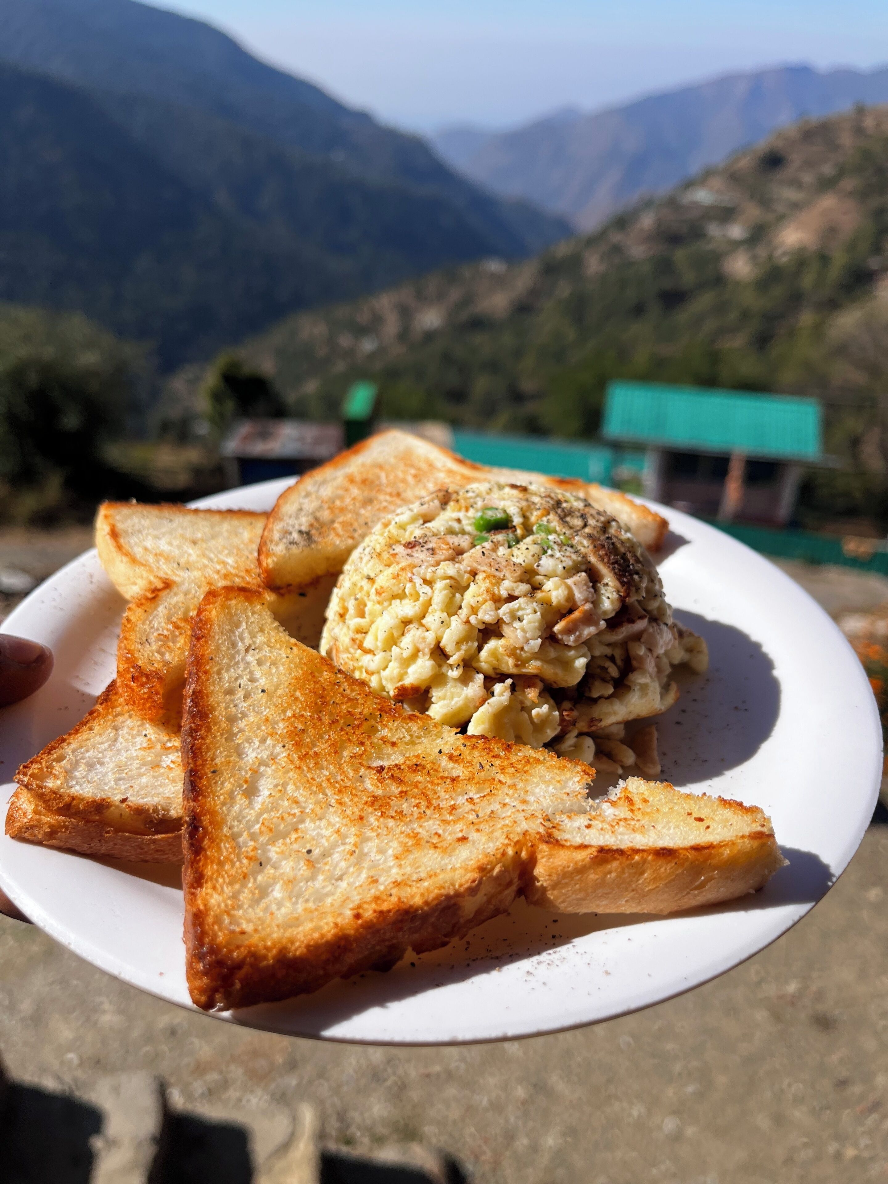 Un piatto con pane tostato e uova strapazzate, su un piatto bianco, con montagne sullo sfondo.