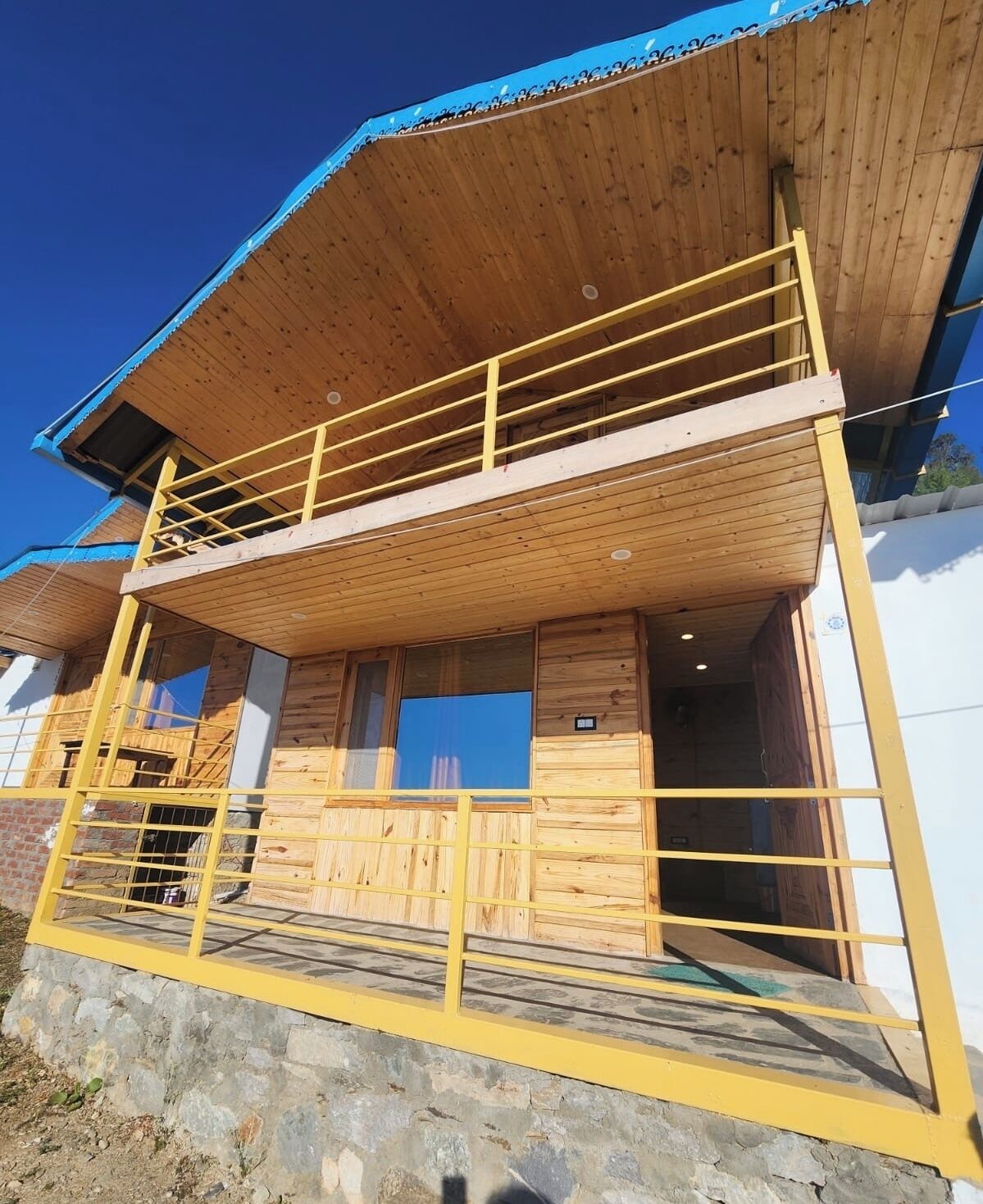 Ein zweistöckiges Holzhaus mit Balkon, Steinuntergrund und blauem Dach.