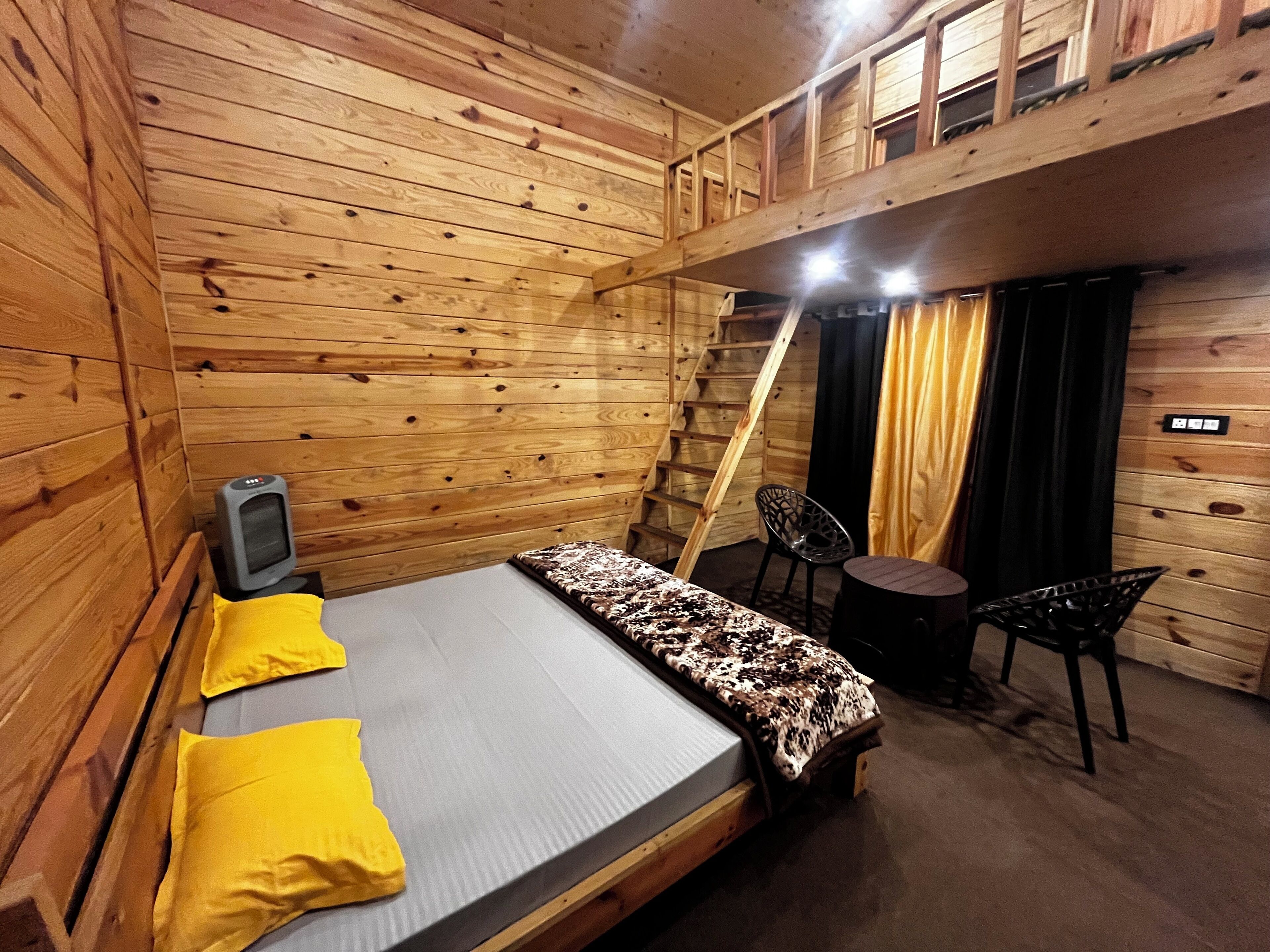 A wooden cabin room with a bed, a chair, a small table, and a heater.