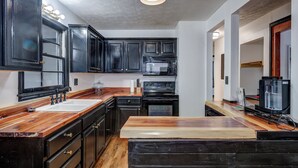 A kitchen with dark cabinets, a wooden countertop, a sink, a microwave, and an oven. - Centralized Modern Home in Johnson City (Johnson City)