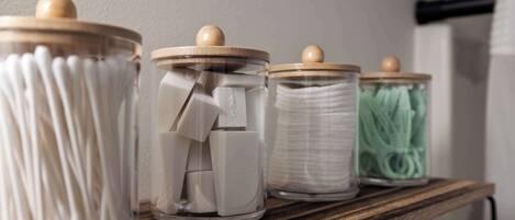 A wooden shelf with three glass jars containing cotton swabs, cotton buds, and a green container.