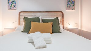 Un lit bien fait, agrémenté d’oreillers blancs et verts, d’un plaid marron et de serviettes blanches. On y trouve deux tables de chevet avec des lampes, ainsi que deux œuvres d’art encadrées accrochées aux murs.