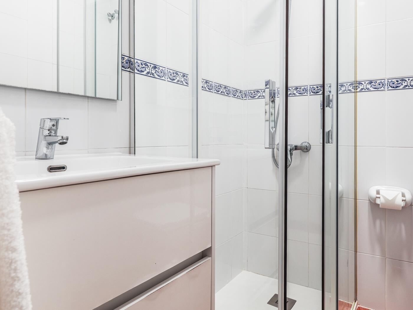 A modern bathroom with a glass shower enclosure, a white sink with a chrome faucet, and a mirror above the sink.