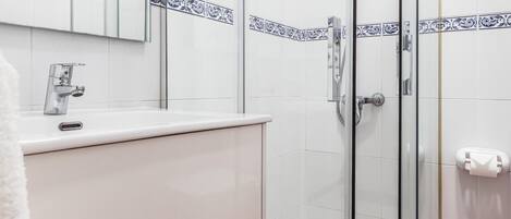 A modern bathroom with a glass shower enclosure, a white sink with a chrome faucet, and a mirror above the sink.