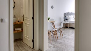 Un baño moderno con inodoro, lavamanos y toallero. Se ve un área de comedor con mesa, sillas y sofá a través de una puerta abierta.