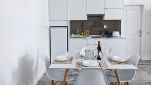 A modern kitchen with white cabinets, a built-in oven, and a dining area with a table set for four. - PB DLX Ilha - Palacete da Baixa (Faro)