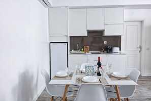 Une cuisine moderne avec des armoires blanches, un four encastré et un coin repas avec une table dressée pour quatre personnes.
