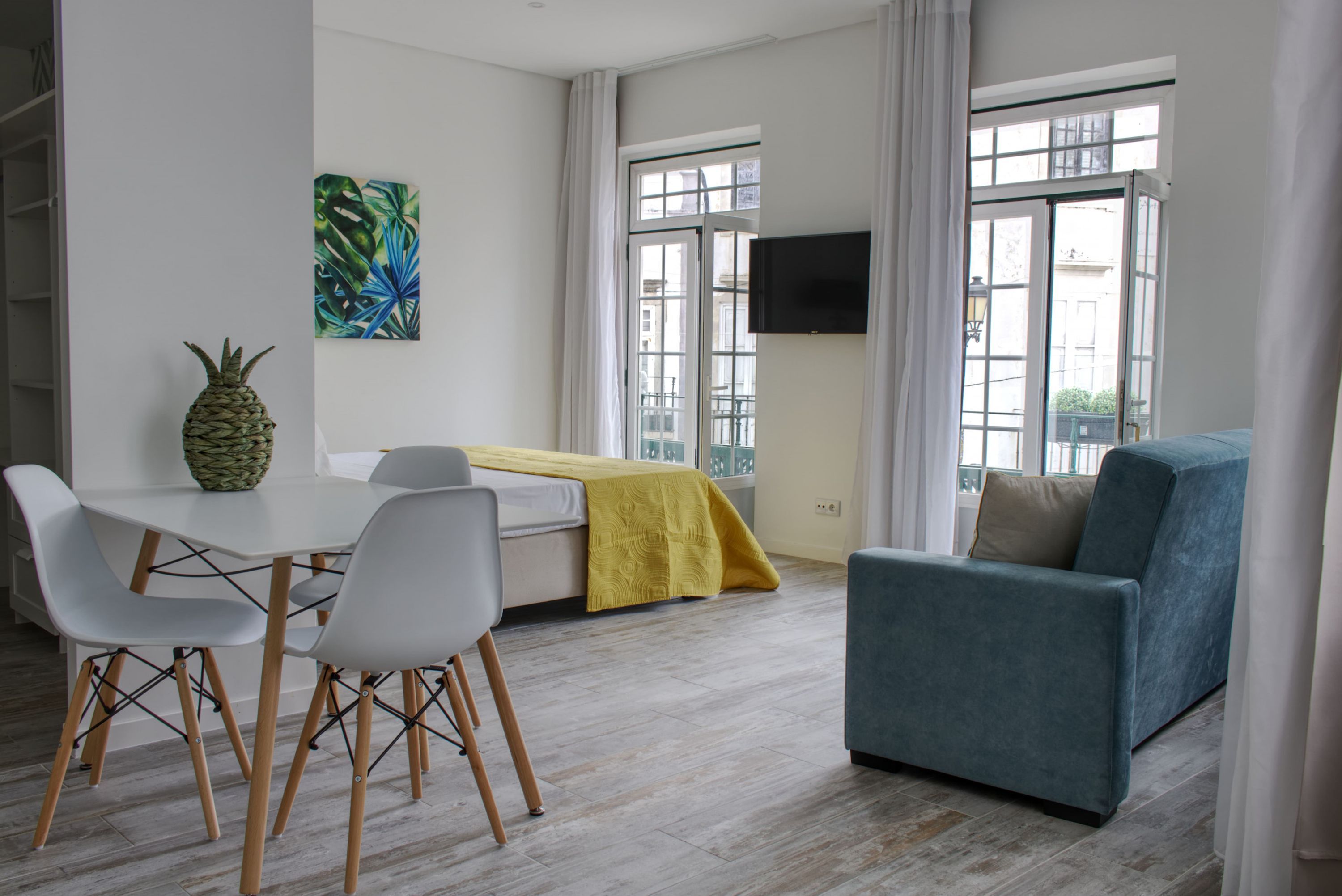 Un salon moderne avec un canapé, une table à manger et des chaises, un téléviseur fixé au mur et une fenêtre avec des rideaux.