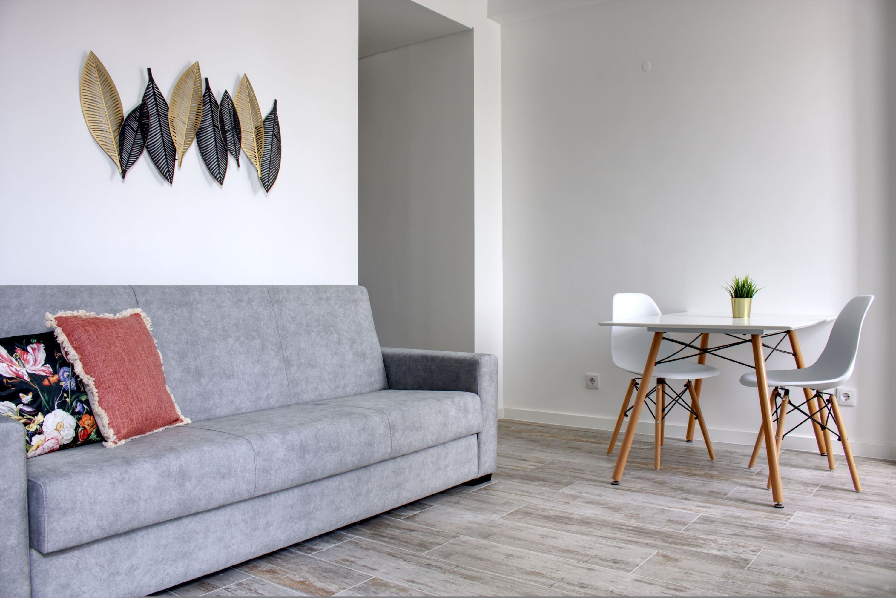 Een moderne woonkamer met een grijze bank, een klein tafeltje met stoelen en decoratieve wandkunst.