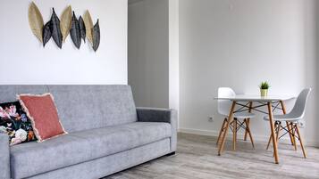 Een moderne woonkamer met een grijze bank, een klein tafeltje met stoelen en decoratieve wandkunst.