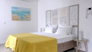 Una habitación de hotel con cama, dos mesitas de noche, un teléfono en la pared y un cuadro.