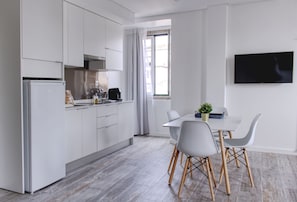 A modern kitchen with white cabinets, a refrigerator, and a dining area with a table and chairs. - PB SUP Ria Formosa - Palacete da Baixa (Faro)