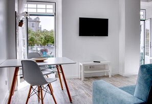Uma sala de estar moderna com área de jantar, uma televisão de tela plana na parede e vista para o horizonte urbano por uma janela grande.