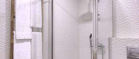 A glass-enclosed shower with a handheld showerhead, white textured walls, and a wooden ladder.